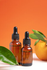 Two bottles different size with orange essential oil for aromatherapy. Orange essential oil. Citrus essential oil on friut background. Hyaluronic acid oil, serum with collagen and peptides.