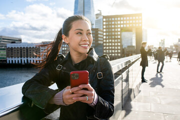 Chinese woman in London smiling and using mobile phone in the city - obrazy, fototapety, plakaty