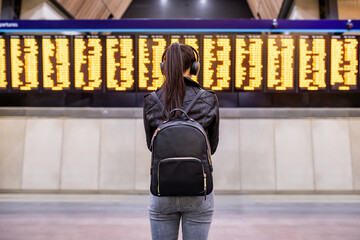 Woman waiting at train station and looking at arrival departure board in London - 540651297