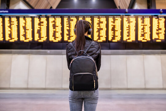 Woman waiting at train station and looking at arrival departure board in London