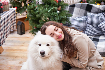 Obraz premium Young woman on background of Christmas tree with white samoyed dog outdoors. Yard decoration for New Year