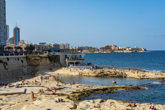 Sunbathers on the Fond Ghadir Beach in Sliema, Malta. In the background is the town of San Giljan (St. Julian&rsquo;s).