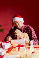 Vet Man in Santa hat and cat in hand making greeting card for New Year and Christmas