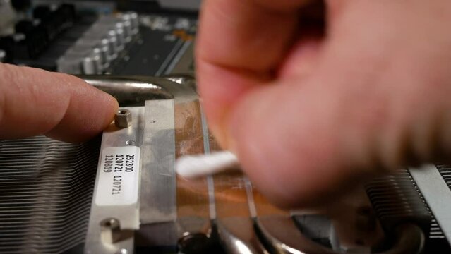 The computer master repairs the video card. Replacing the thermal paste in the video card. The master removes the old, dried thermal paste from the cooling radiator. Close-up, selective focus.