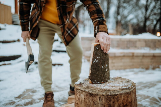 Low section of man chopping wood outdoor during snowy winter.