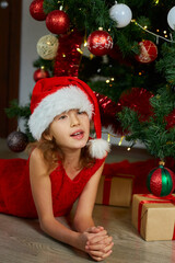 Happy Girl in Santa hat lying near christmas tree at home.