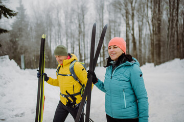 Senior couple crossing forest with skis in hands.
