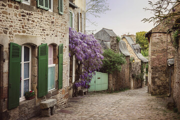 Picturesque street of the medieval town of Dinan in spring in France, Brittany. Blooming wisteria on a medieval street. The fabulous city of Dinant, a popular tourist destination in France