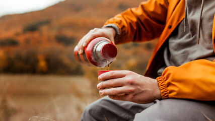 young man in a yellow jacket drinking hot tea from a thermos