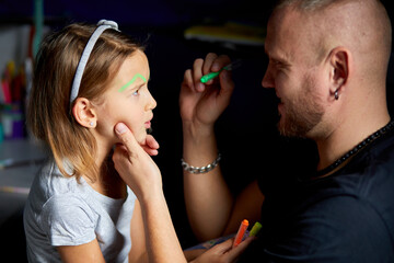 Daughter and father paint a face, having fun, leisure together at home