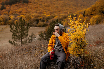 Naklejka na ściany i meble young man in a yellow jacket drinking hot tea from a thermos at the autumn forest