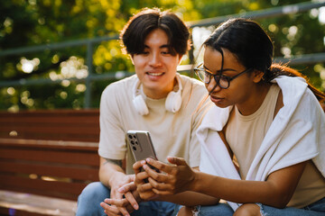 Two multiracial friends using mobile phone together in skate park