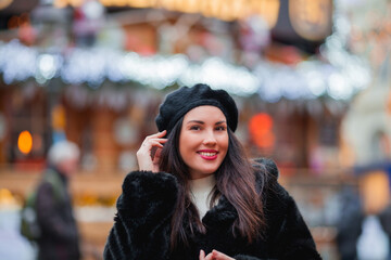 Fototapeta premium Beautiful dark-haired young woman in an eco fur coat walks around the city and does Christmas shopping. New Year holidays. Present. Holidays. Winter.