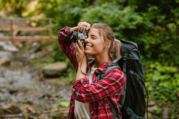 Happy white woman taking photo on camera while hiking in forest