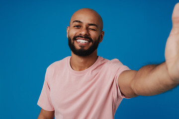 Black bald man with beard winking while taking selfie photo