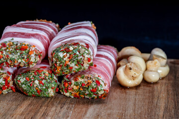 Bacon-wrapped meat roll with spices and herbs. Jamon pork, prosciutto, or presunto meat products, tartare meat inside. Meatloaf close up high focus view with shallow depth of field on a wooden board