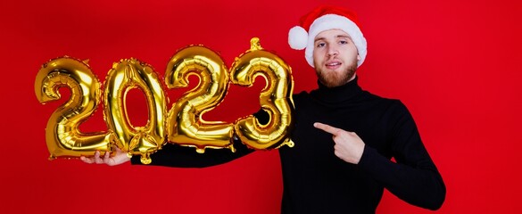 A smiling man in a Santa Claus hat looks into the camera and holds the shiny numbers of the new...