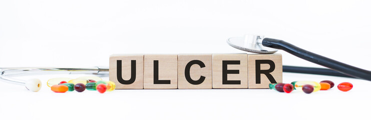 Word ULCER building from wooden cubes on a light background near the stethoscope and tablets