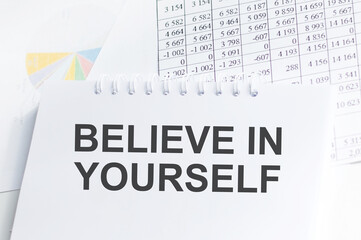 BELIEVE IN YOURSELF text on blue wooden background with charts