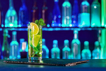 Cocktail with ice on bar counter in a restaurant, pub. Orange drink with juice. Fresh prepared alcoholic cooler beverage at nightclub. Showcases with bottles on dark background