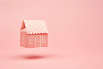 Pink paper house model hovering above the surface of the bright solid pink fond background. Real...