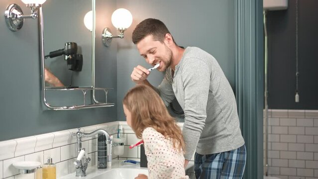 Close up of handsome caring father brushing teeth in bathroom with small kid girl. Caucasian dad teaching his cute little daughter to brush teeth using toothbrush in sink. Healthy hygiene.