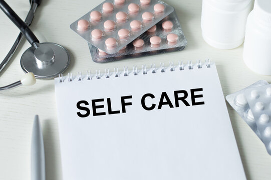 Self Care text text on a notebook on a table next to medicine, stethoscope, medical concept