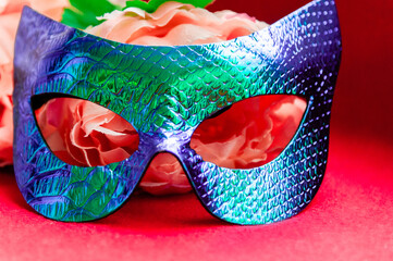  masquerade mask  on  red background next to artificial flowers. look at the camera. closeup