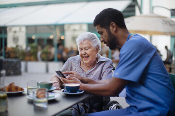 Caregiver having coffee with his client and learning her using smartphone, outdoor at cafe.