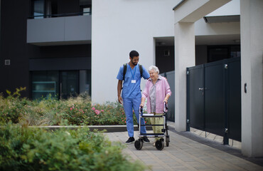 Caregiver walking with senior woman client in front of nurishing home.