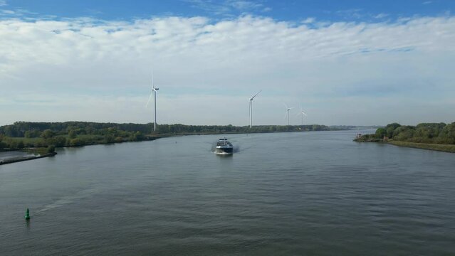 Aerial footage of cargo ship moving on wide river. Row of wind power stations along riverbank. Transport and logistics concept. Barendrecht, Netherlands