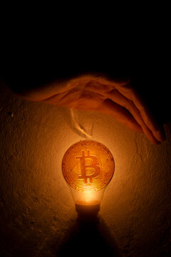 Hand Blocking The Light From The Light Bulb With Bitcoin Coins. Business Money Protection Concept.