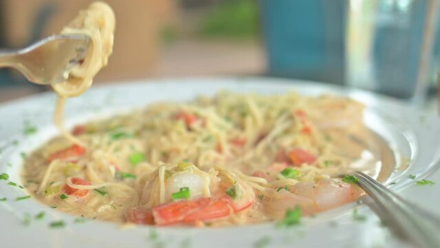 Person twirling spaghetti pasta on a fork. Pasta dish with shrimp and creamy sauce.