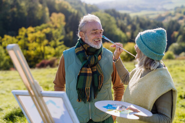 Senior couple painting together in nature, during autumn day.