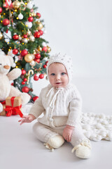 Santa baby. Christmas tree background. Happy New Year! Child in knitted suit