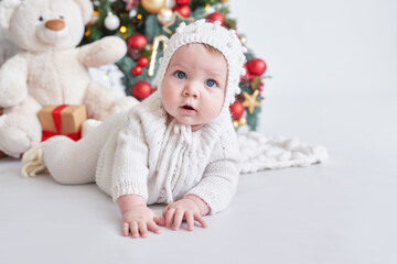 Santa baby. Christmas tree background. Happy New Year! Child in knitted suit