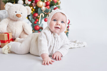 Santa baby. Christmas tree background. Happy New Year! Child in knitted suit