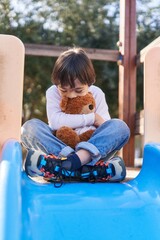Down syndrome kid smiling confident playing with teddy bear on slide at park