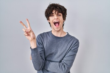 Young man standing over isolated background smiling with happy face winking at the camera doing...