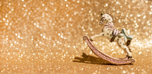 Festive composition. Vintage rocking horse figurine standing on a sparkling gold background....