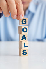 Businesswoman placing wooden blocks on top of each other. "Goals" written on wooden blocks.