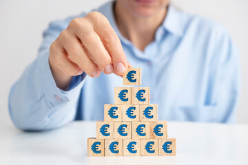 Businesswoman placing wooden block pyramid, euro signs on wooden blocks.