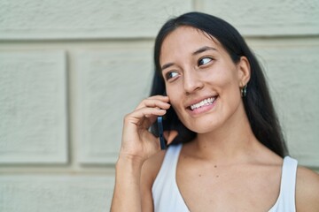 Young beautiful hispanic woman smiling confident talking on the smartphone over isolated white brick background