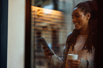 Woman drinks coffee and use mobile phone at home.