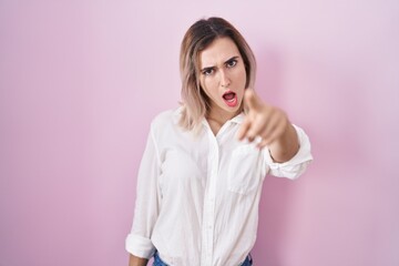 Young beautiful woman standing over pink background pointing displeased and frustrated to the camera, angry and furious with you