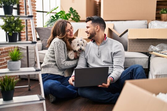 Man and woman using laptop sitting on floor with dog at new home