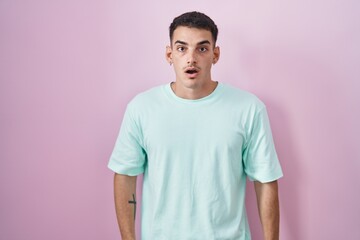 Handsome hispanic man standing over pink background afraid and shocked with surprise and amazed expression, fear and excited face.