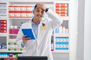 Handsome hispanic man working at pharmacy drugstore with tablet stressed and frustrated with hand...