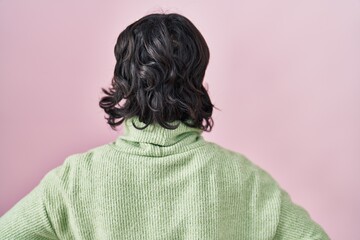 Young beautiful woman standing over pink background standing backwards looking away with arms on body