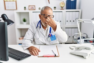 Mature doctor man at the clinic tired rubbing nose and eyes feeling fatigue and headache. stress and frustration concept.